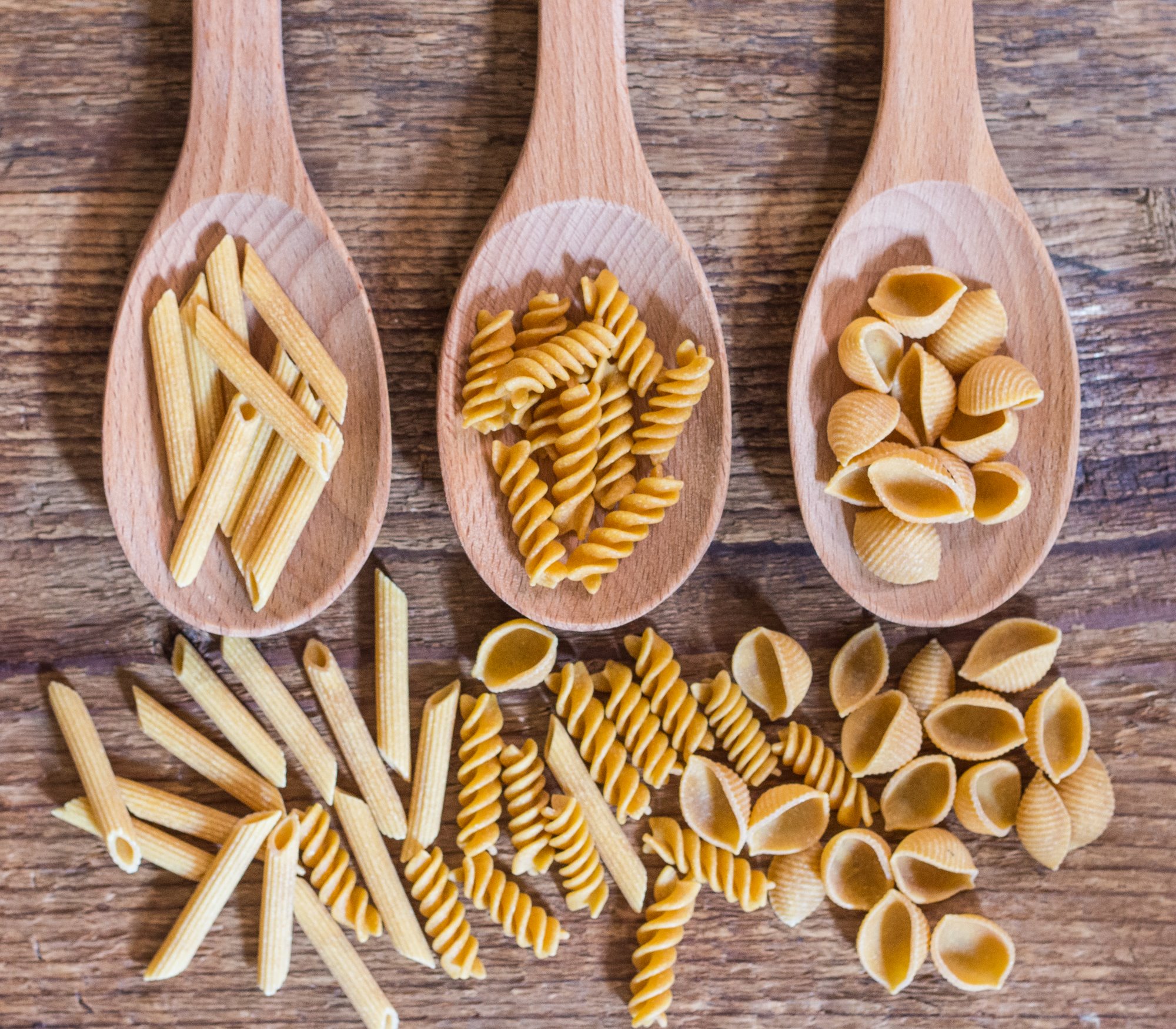 dried pasta in different shapes on wooden spoons